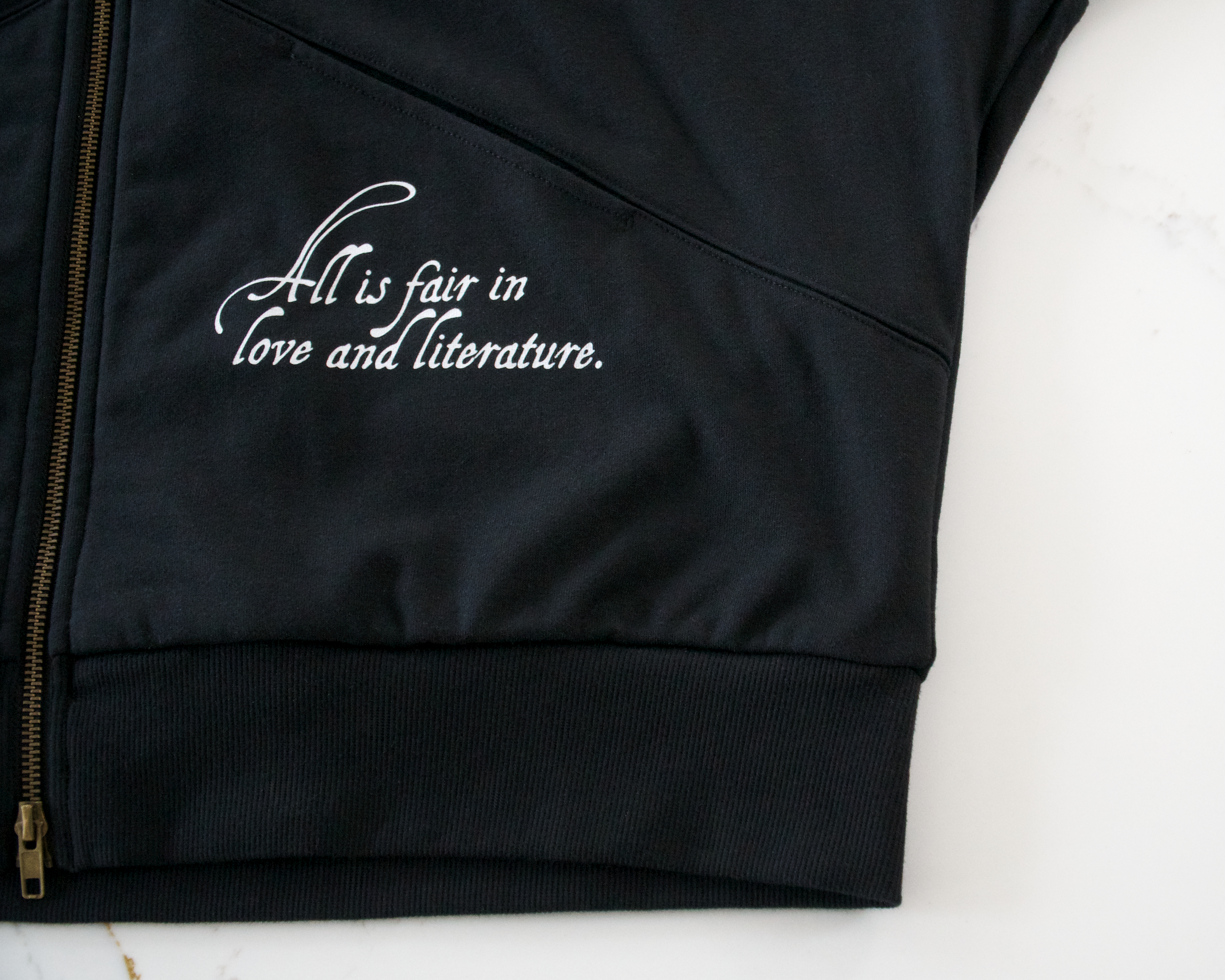 Close-up of “All Is Fair in Love & Literature” text printed on black zip hoodie fabric
