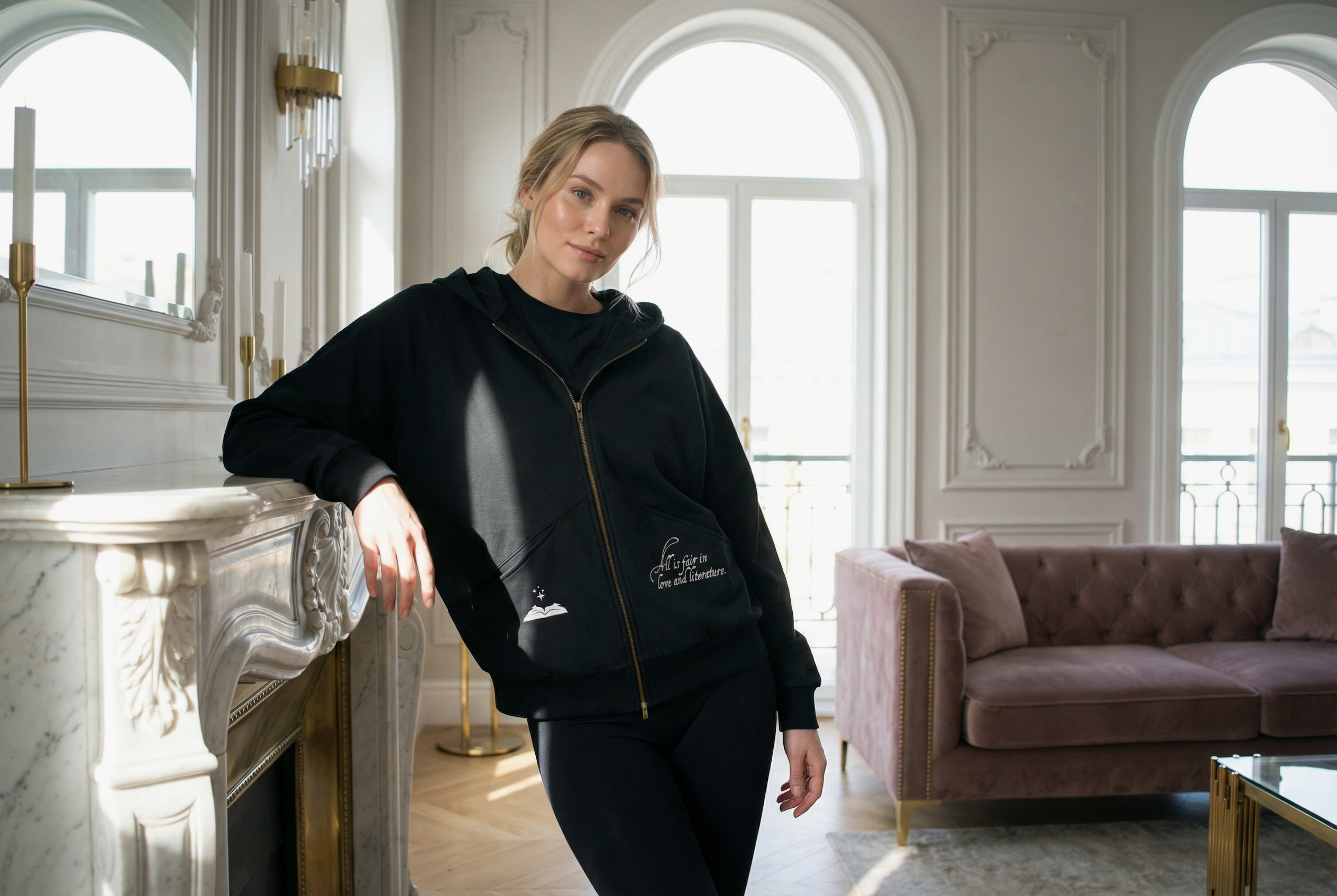 Model styling a black zip-through hoodie with literary quote design in a light-filled room with a cozy, neoclassical aesthetic