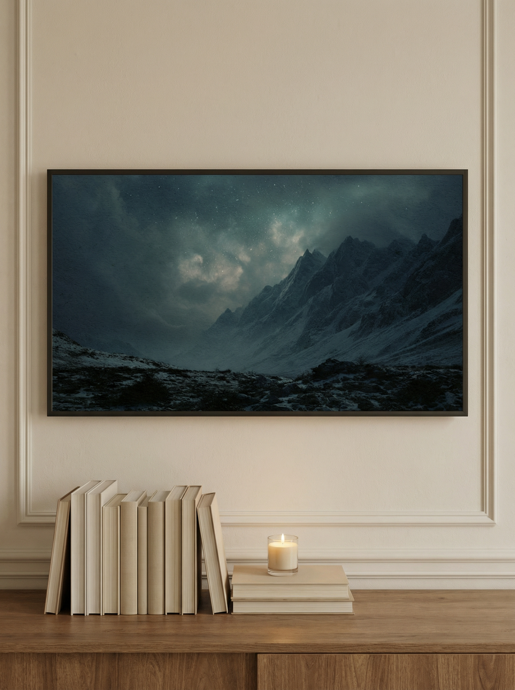 Frame TV artwork featuring a glowing night sky above jagged snowy peaks styled on a wooden console with books and a candle.
