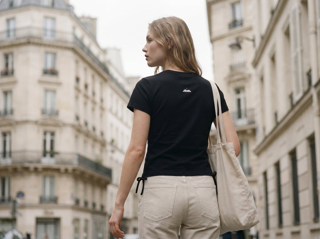 Woman walking on a city street wearing a black t-shirt and beige pants.