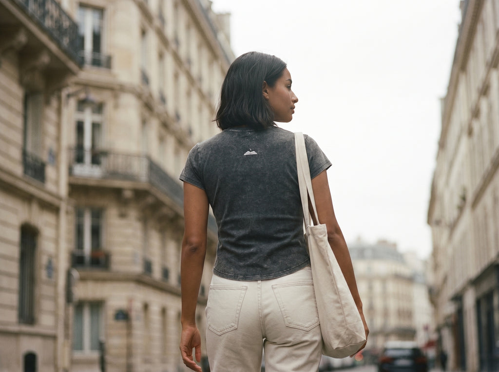 Woman walking down a city street holding a beige tote bag. Charcoal grey t shirt with a gleam logo on the back 