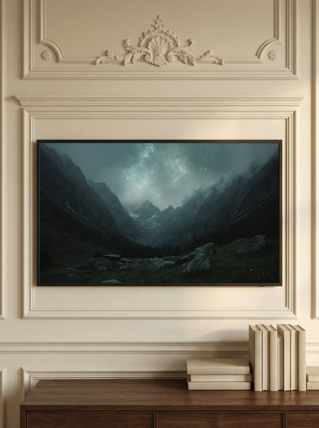 Frame TV artwork featuring a glowing night sky above jagged snowy peaks styled on a wooden console with books and a candle.